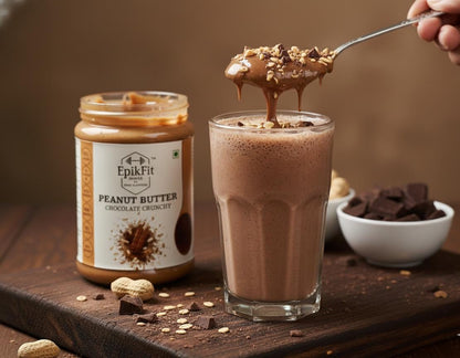 Glass of chocolate milk with a spoonful of EpikFit Peanut Butter Chocolate Crunchy on a wooden surface.