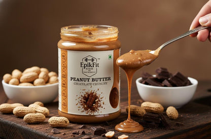 Jar of EpikFit Peanut Butter Chocolate Crunchy with a spoonful being lifted, surrounded by peanuts and chocolate pieces on a wooden surface.