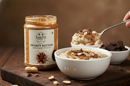 Jar of EpikFit Peanut Butter Chocolate Crunchy on a wooden surface with bowls of dessert.
